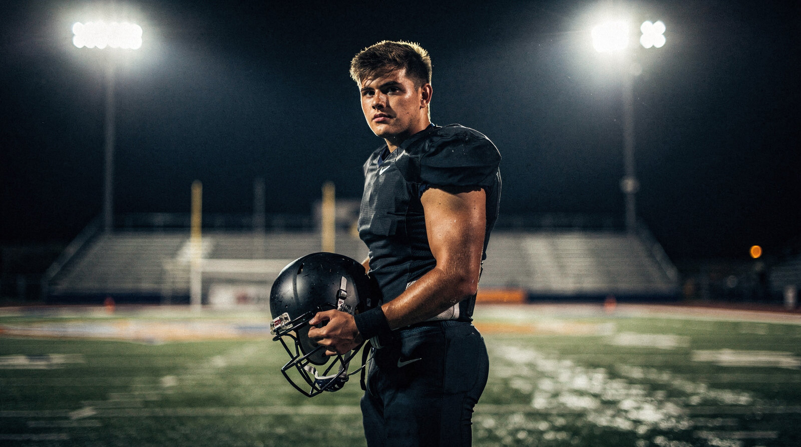 Football player holding his helmet on an empty field under the stadium lights at night